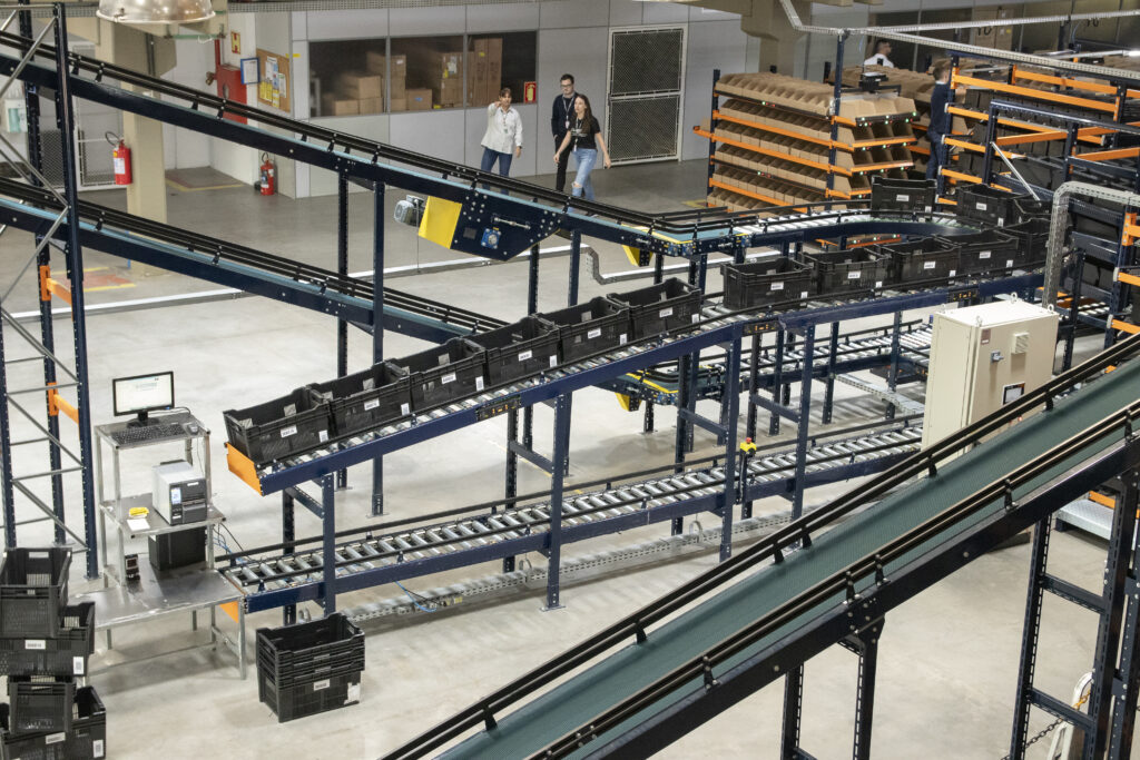 Sistema automatizado de armazenagem com esteiras industriais e transportadores integrados para picking e movimentação de caixas em centro logístico.
