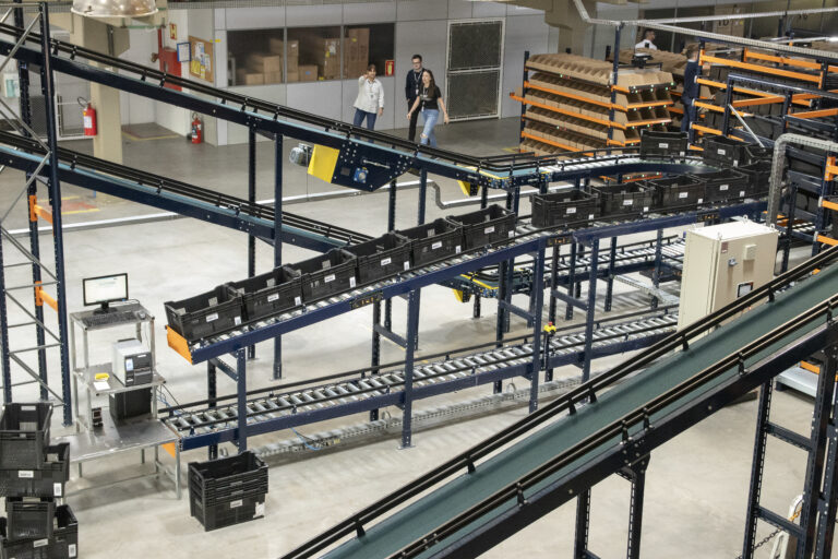 Sistema automatizado de armazenagem com esteiras industriais e transportadores integrados para picking e movimentação de caixas em centro logístico.