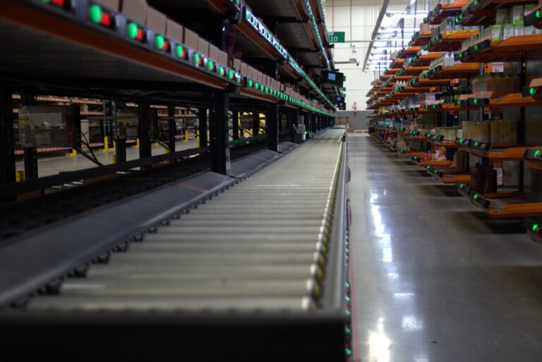 Linha automatizada de picking com sinalização Pick-to-Light e esteira transportadora em operação logística industrial.