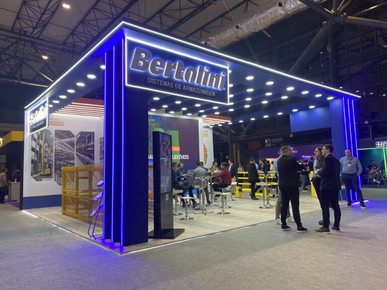 A imagem mostra o estande da Bertolini Sistemas de Armazenagem na Feira Logistique 2025. O estande é azul e branco. Várias pessoas aparecem conversando no interior e na frente dele.