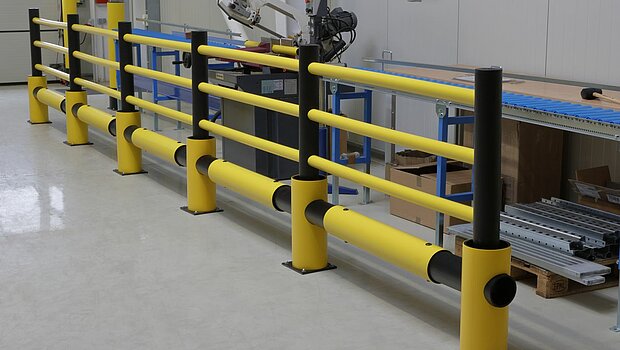 Barreiras de proteção flexíveis fixadas ao solo em um centro logístico, posicionadas para evitar impactos em colunas e áreas de tráfego.